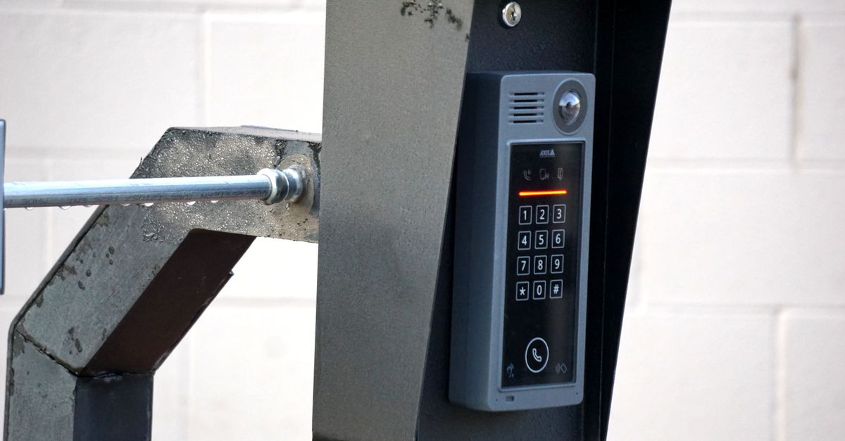 Close-up of a modern security intercom and keypad mounted on a wall outdoors with visible wiring.