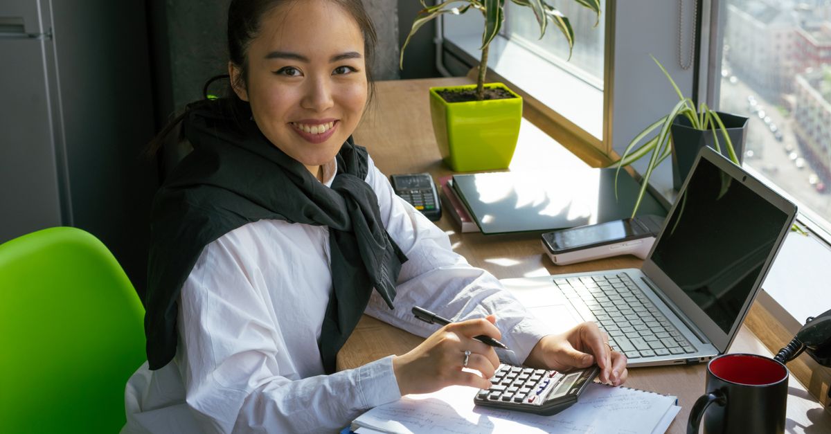 Confident woman working with calculator in bright office setting, surrounded by office tools.