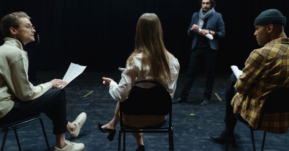 Group of actors in rehearsal with director, practicing for a theater performance.