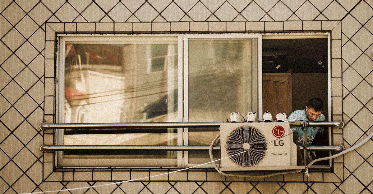 Man looks outside a window with an LG air conditioner unit visible, creating a reflective effect.