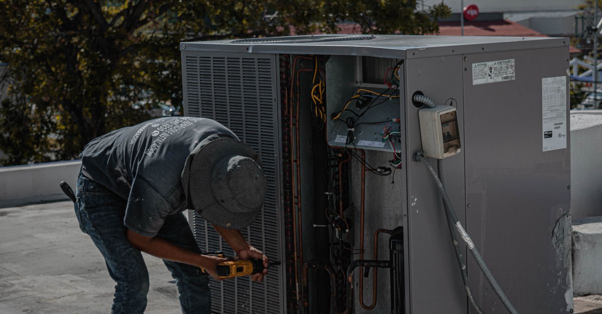 A technician is repairing an air conditioning unit on a rooftop, demonstrating skilled manual work.