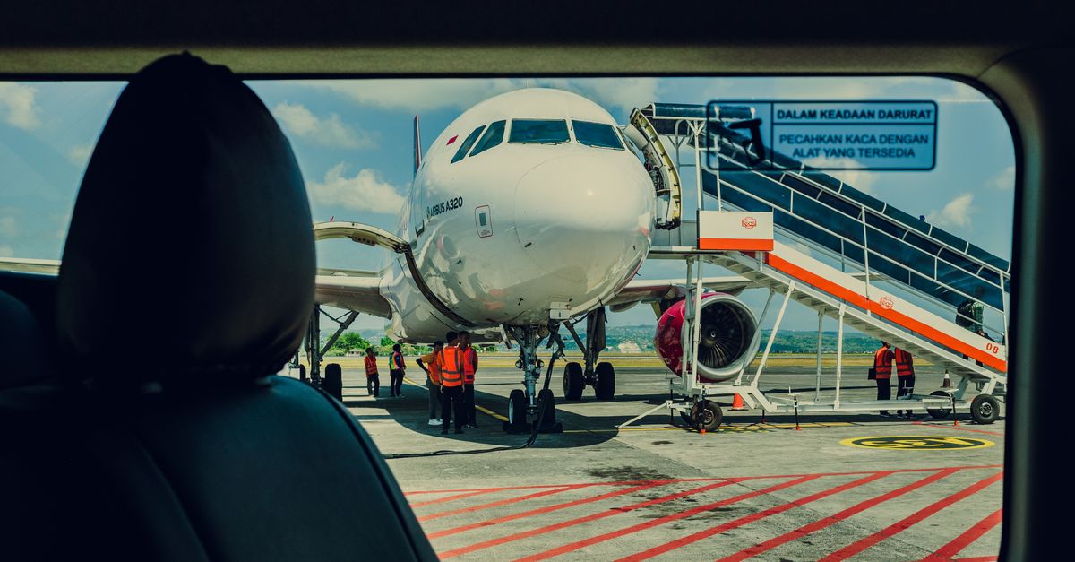 Airplane viewed from a car, parked on the tarmac at an airport with crew working nearby.