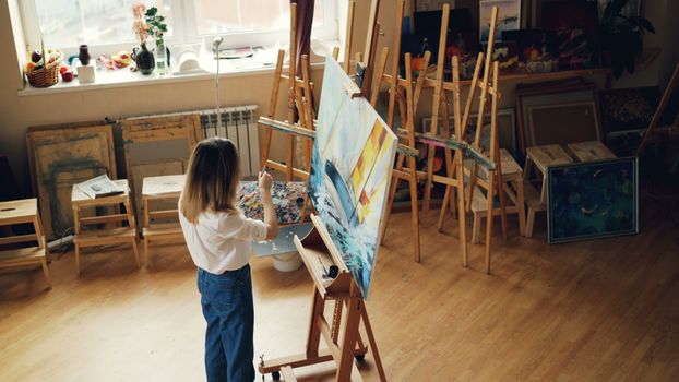 A woman artist paints on a canvas in a bright, well-equipped studio.