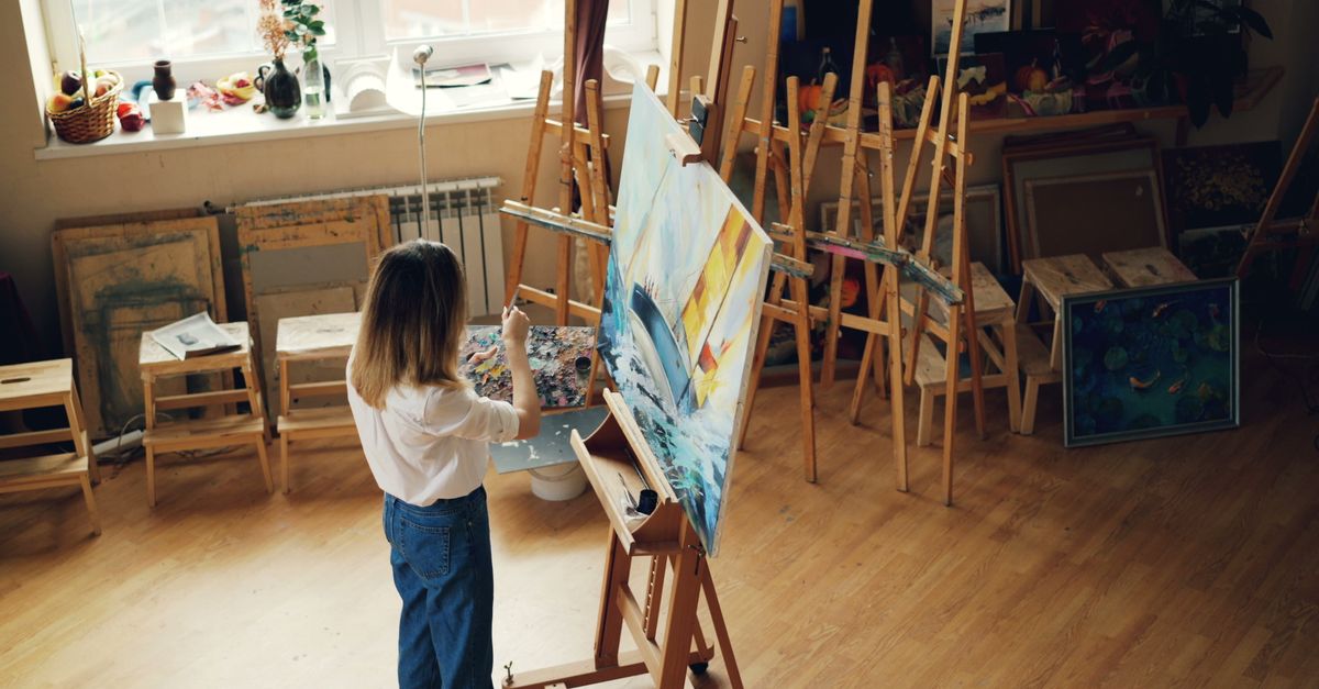 A woman artist paints on a canvas in a bright, well-equipped studio.