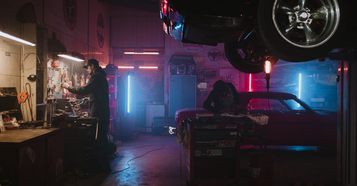 Mechanics working in a neon-lit garage, focusing on tools and car repairs under vibrant lights.