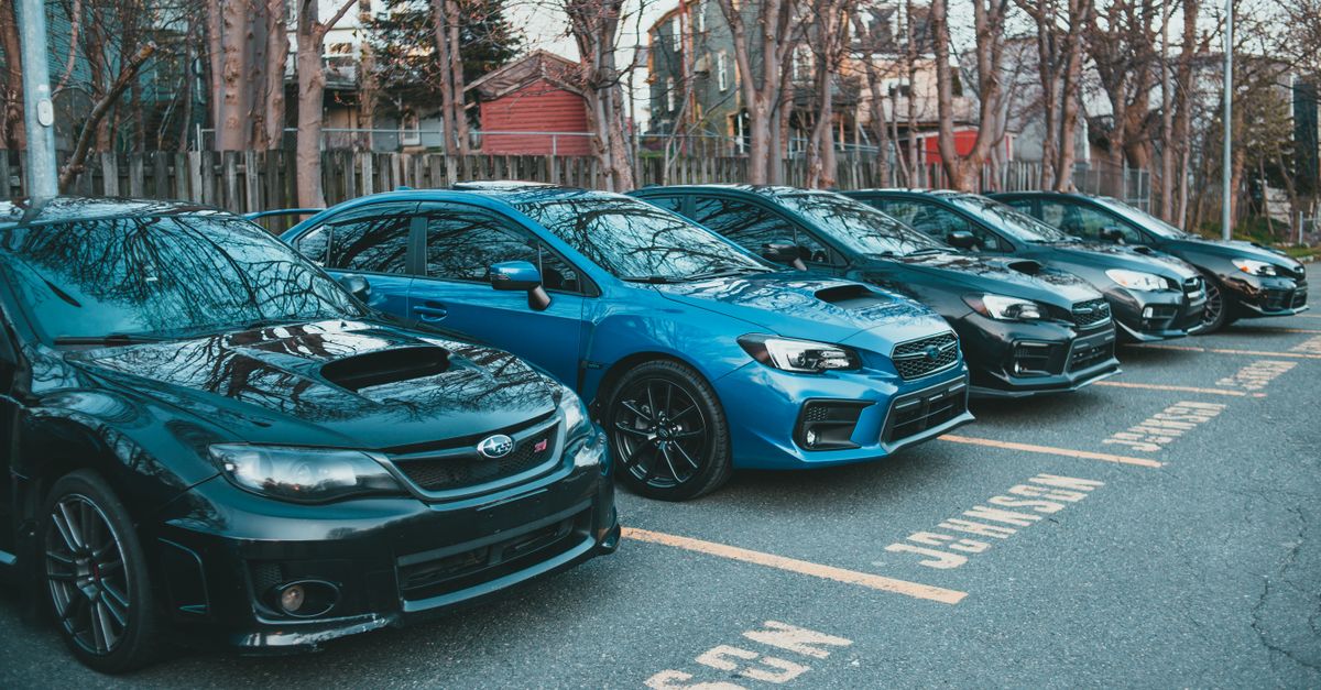 Multiple Subaru cars parked in an outdoor lot lined with trees, showcasing automotive design.