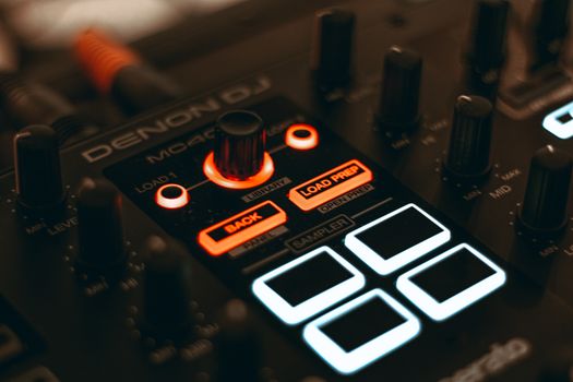 A detailed close-up of a DJ audio mixer with illuminated LED buttons and knobs.