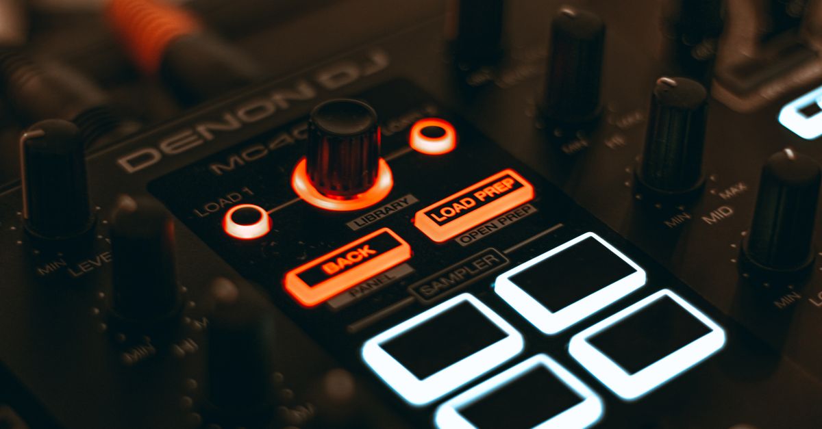 A detailed close-up of a DJ audio mixer with illuminated LED buttons and knobs.