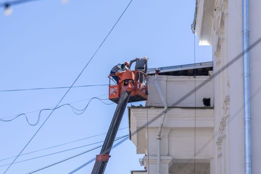 Workers on lift repairing building façade under clear sky.