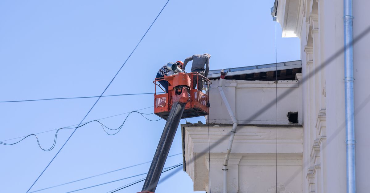 Workers on lift repairing building façade under clear sky.