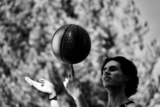 Black and white image of a basketball being spun on a finger outdoors.