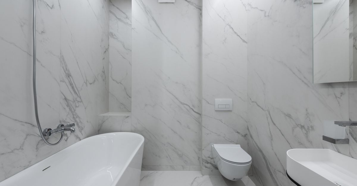 Interior of stylish bathroom with marble walls and bath placed near toilet and ceramic sink in light room with mirror
