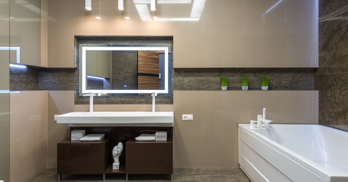 White bathtub placed near cabinet with sink at wall with mirror in light stylish bathroom with glowing illumination in apartment