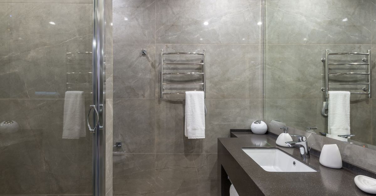 Interior of modern minimalist bathroom with glass shower cabin and shiny tiled walls reflecting in big mirror hanging above sink