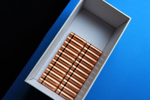 Top view of neatly arranged batteries in a box on a contrasting blue surface.