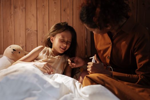 A caring mother comforts her sick daughter in a cozy bedroom setting.