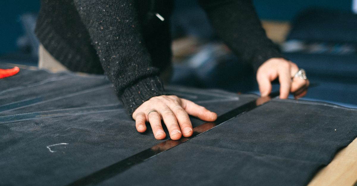 Faceless crop male designer standing at workbench with ruler and measuring piece of textile while working in atelier
