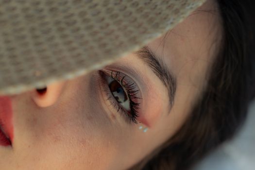 Detailed close-up of a woman's eye shaded by a sun hat, featuring makeup and jewels.