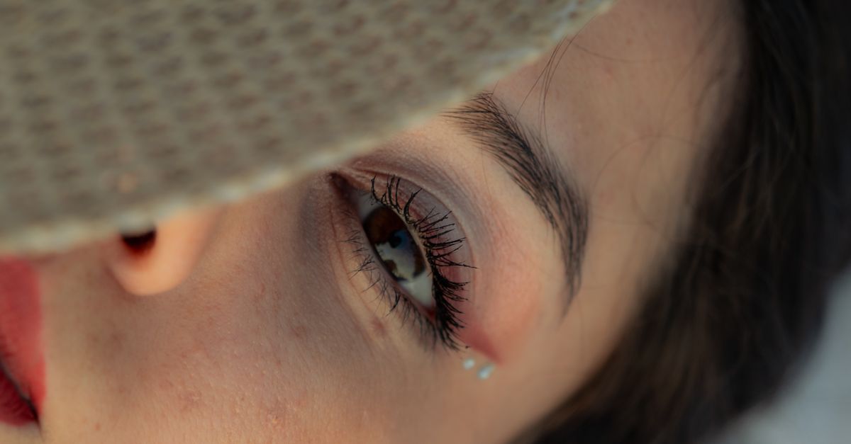 Detailed close-up of a woman's eye shaded by a sun hat, featuring makeup and jewels.
