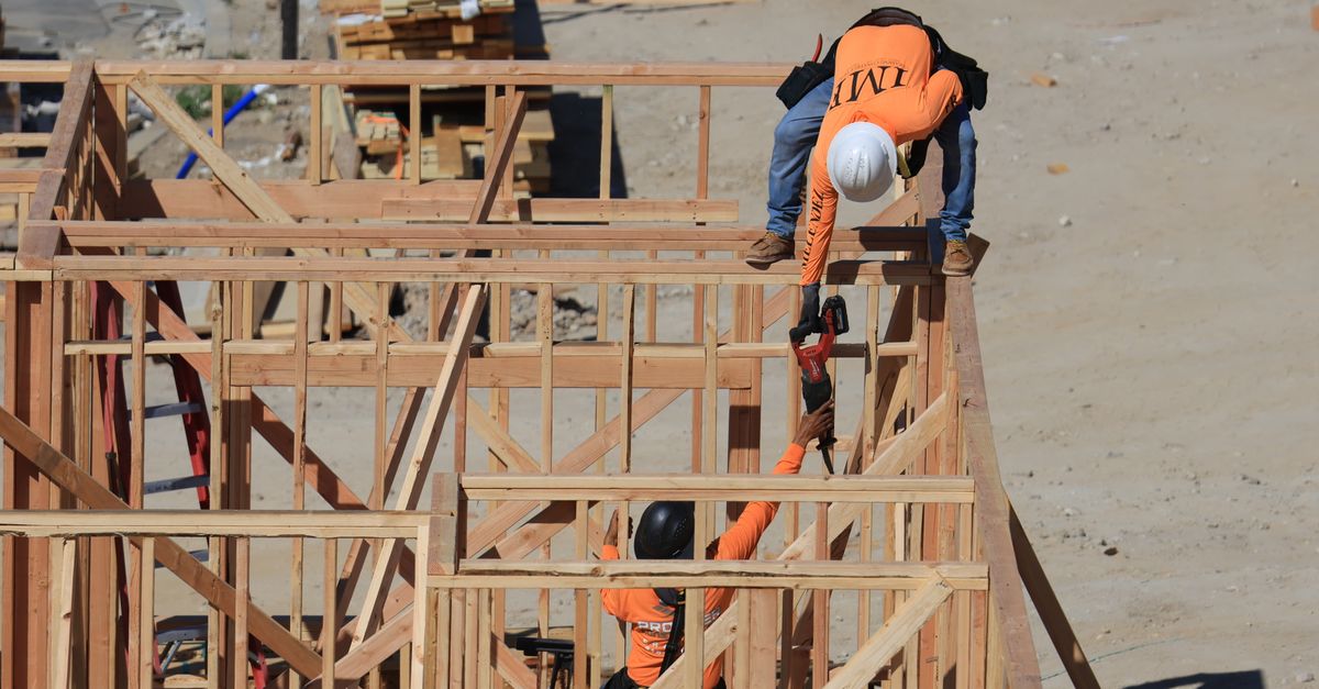 Two construction workers framing a wooden structure outdoors at a building site.