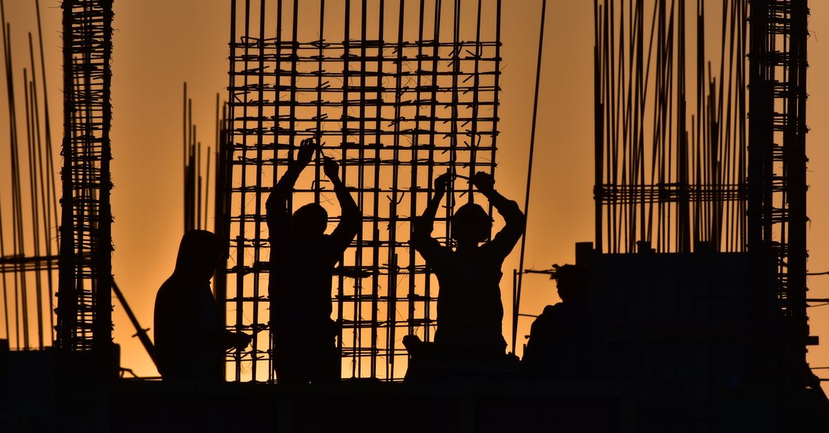 Silhouetted construction workers at a site during sunset, creating a dramatic scene.