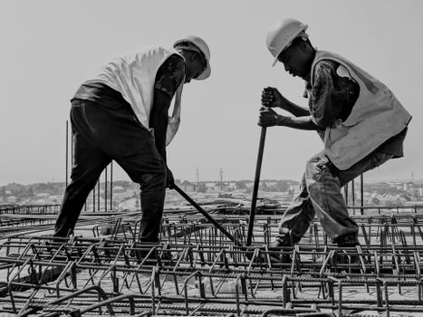 Black and white image of two construction workers reinforcing steel bars on a building site.