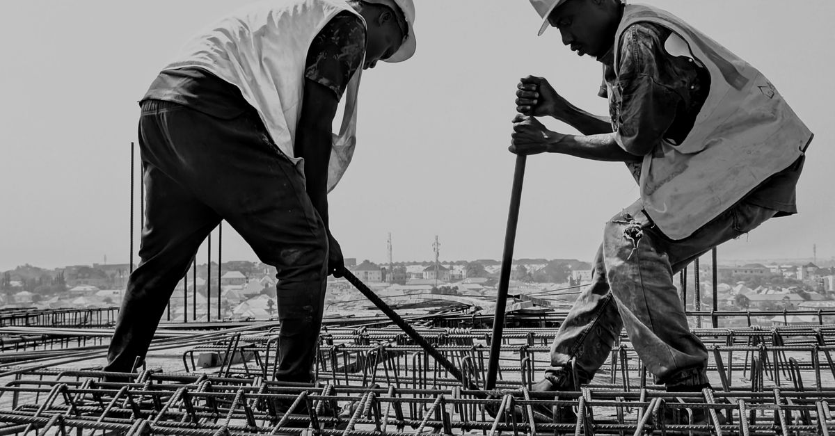 Black and white image of two construction workers reinforcing steel bars on a building site.