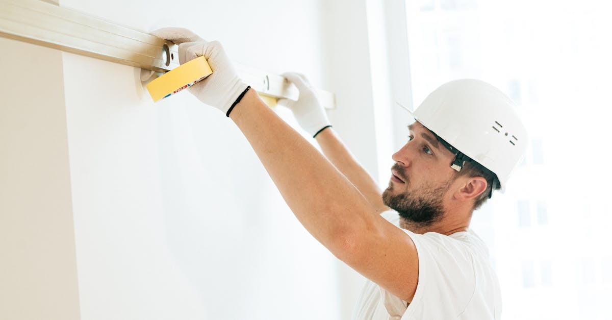 A construction worker measures a wall with a spirit level indoors.
