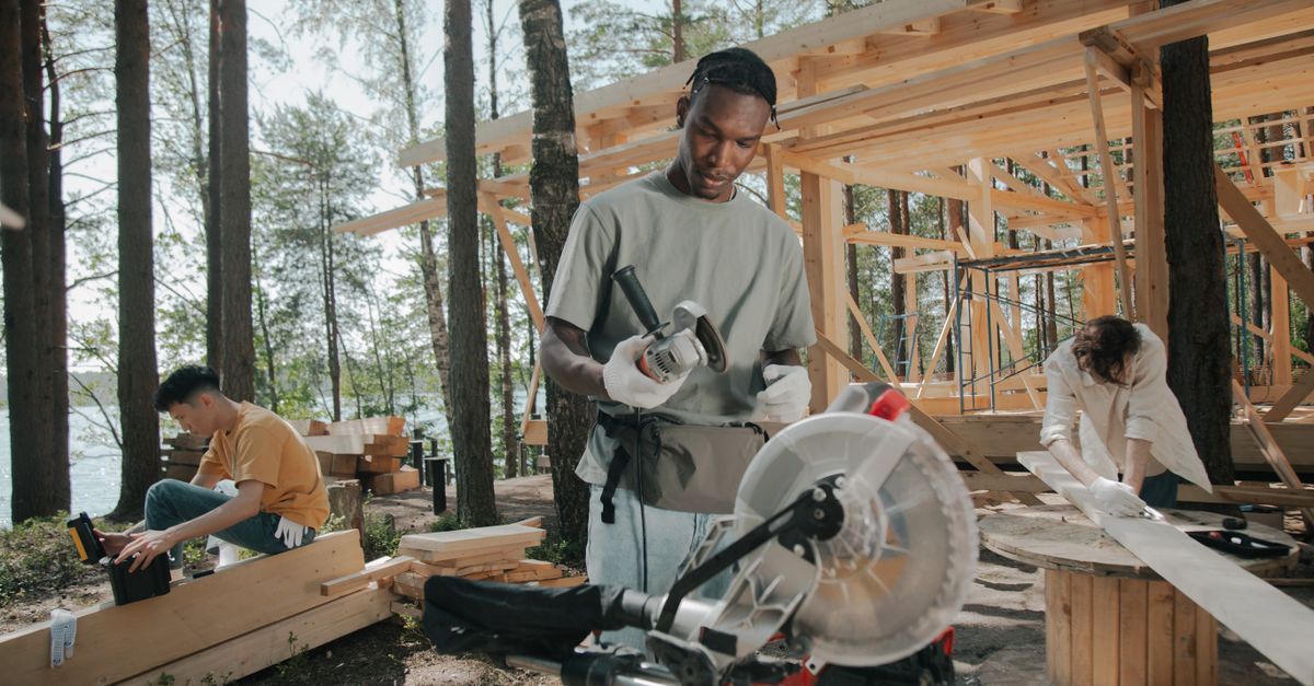 Construction crew building a wooden structure outdoors in a forest setting.