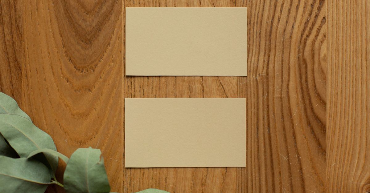 Top view of mock up yellow business cards placed on wooden surface near plant with green leaves in light room