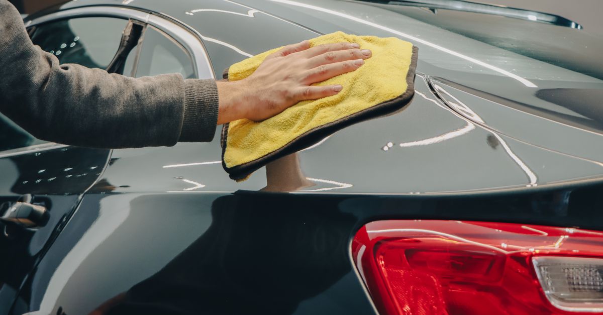 Close-up of hand polishing a shiny car with a yellow cloth indoors.