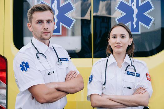 Portrait of two paramedics with stethoscopes standing confidently in front of an ambulance.