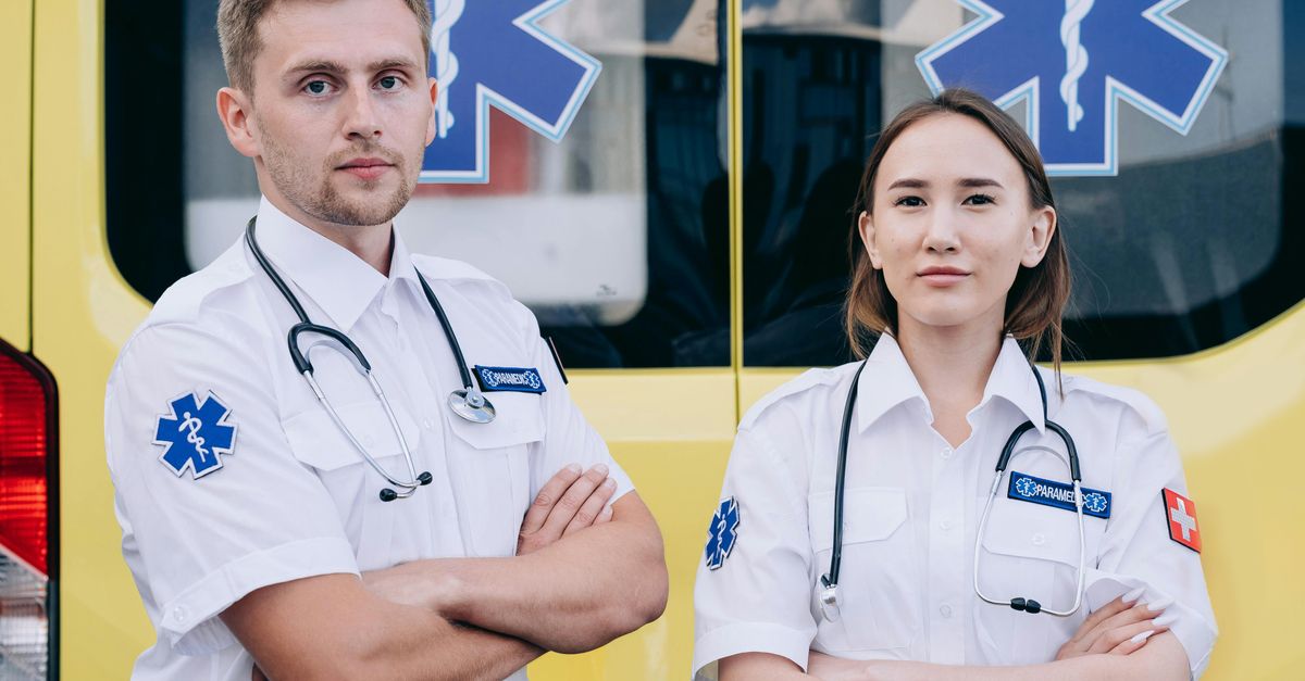 Portrait of two paramedics with stethoscopes standing confidently in front of an ambulance.