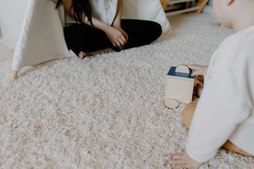 A child plays with a wooden block toy on a cozy carpet indoors, creating a warm family moment.