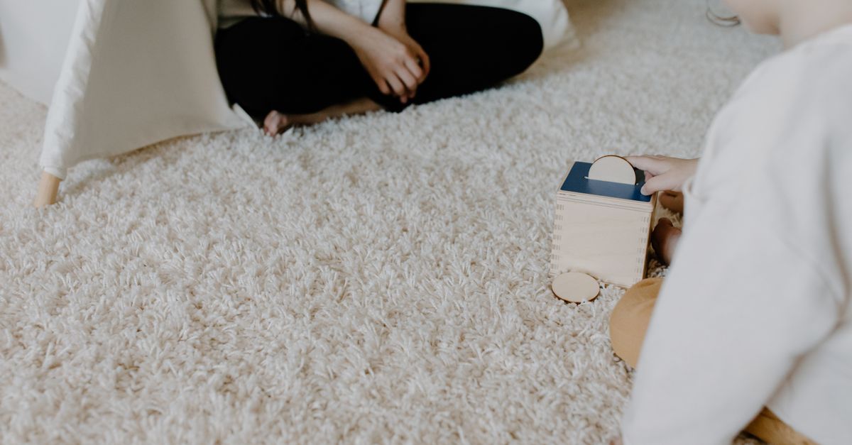 A child plays with a wooden block toy on a cozy carpet indoors, creating a warm family moment.