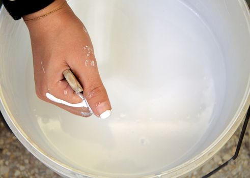 Close-up of a hand mixing white paint with a stick inside a bucket in Fès, Morocco.