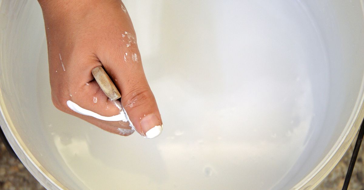 Close-up of a hand mixing white paint with a stick inside a bucket in Fès, Morocco.