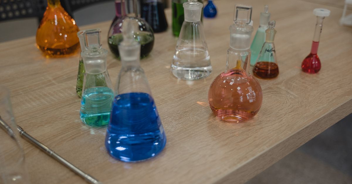 Colorful laboratory flasks with various liquids on a wooden desk for science experiments.