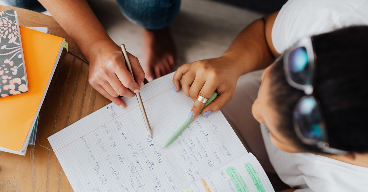 Two students studying together with notebooks and pens, viewed from above.