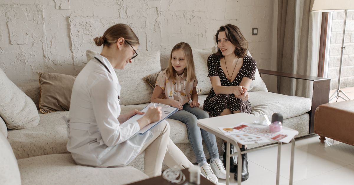 A doctor consults with a mother and daughter in a cozy indoor setting.