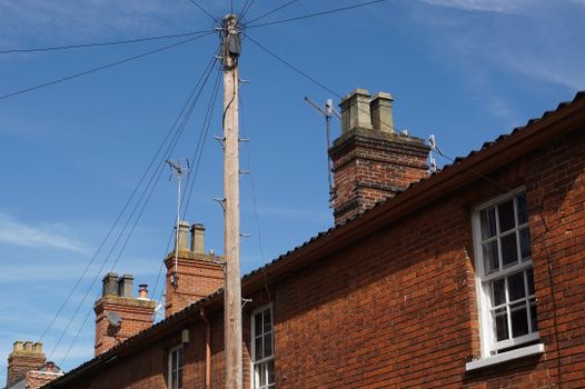 A brick building featuring chimneys and an electric post under a clear blue sky.