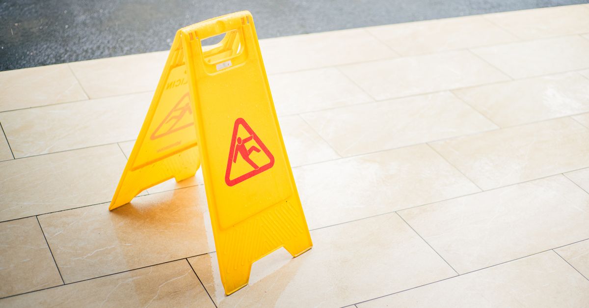 A bright yellow caution sign placed on a tile floor indicating a wet area for safety.