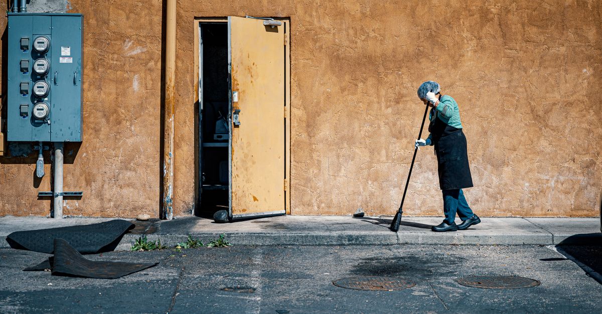 Person sweeping outdoors on a city sidewalk in bright daylight.