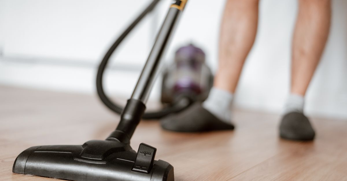 Crop anonymous male in slippers washing floor with vacuum cleaner in flat during household routine