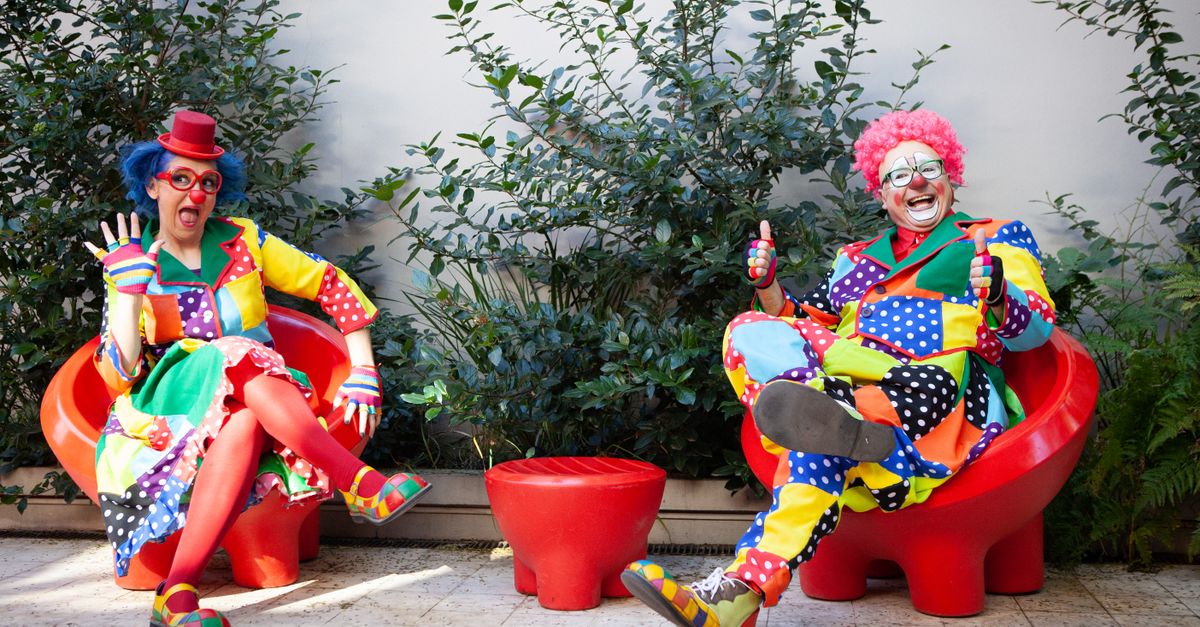 Vibrant clowns in colorful costumes sitting outside with red chairs, spreading joy and humor.