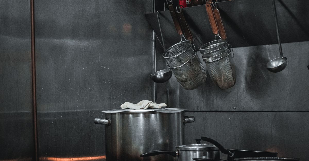 Stainless steel commercial kitchen setup with pots, strainers, and utensils hanging on a rail.