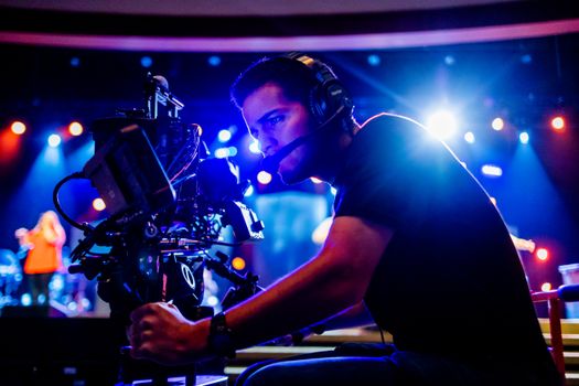 Focused cameraman using advanced equipment at a vibrant stage event, under colorful stage lights.