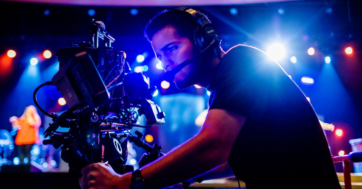 Focused cameraman using advanced equipment at a vibrant stage event, under colorful stage lights.