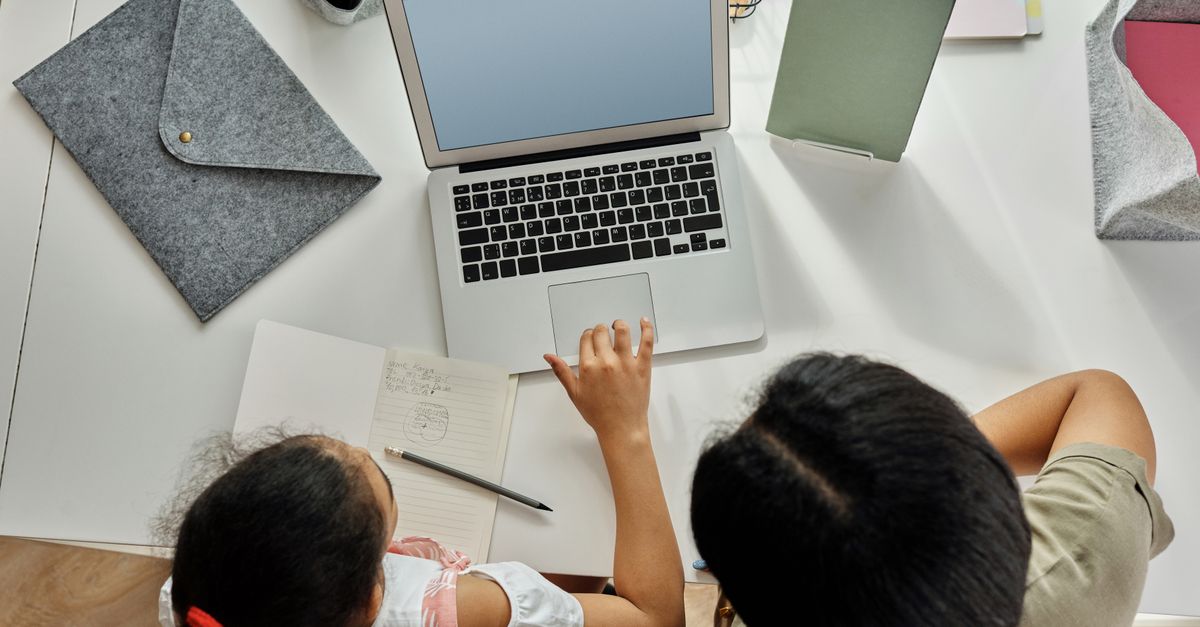 A mother helps her daughter with schoolwork on a laptop at home, promoting education and bonding.