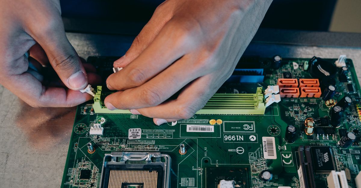Hands carefully assembling a computer motherboard, showcasing technical craftsmanship in electronics.